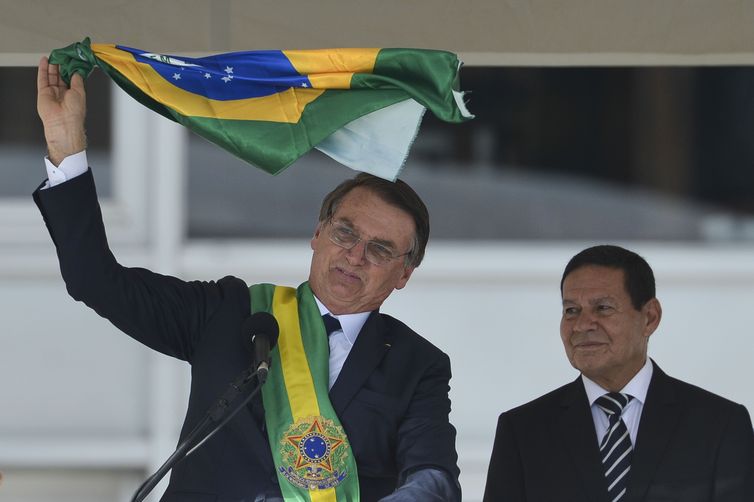 Presidente Jair Bolsonaro e o vice-presidente Hamilton Mourão exibem uma bandeira nacional durante discurso no parlatório do Palácio do Planalto.