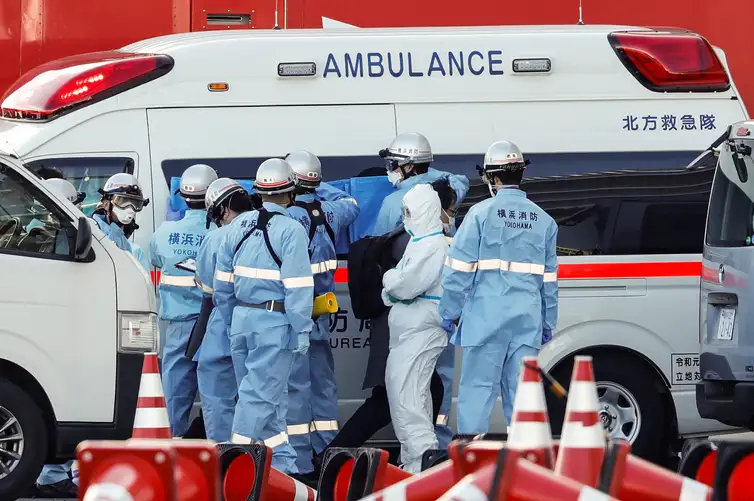Firefighters wearing protective gear hold canvas up to the windows of an ambulance to protect the privacy of passengers, who tested positive for coronavirus, before they are transferred from the cruise ship Diamond Princess to a hospital, after