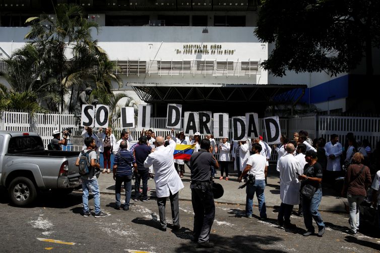 Venezuelanos, incluindo os médicos, seguram faixas que dizem &quot;Solidariedade&quot; enquanto se reúnem em frente a um hospital público infantil durante um apagão em Caracas, Venezuela.