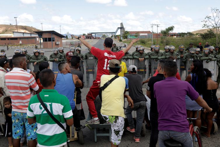 Pessoas esperando para atravessar para a Venezuela em frente aos guardas nacionais venezuelanos na fronteira entre a Venezuela e o Brasil em Pacaraima.