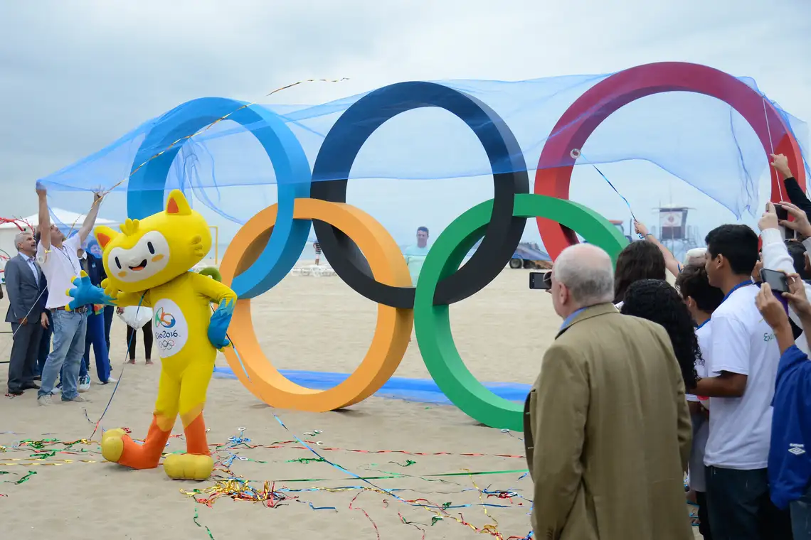 Tomaz Silva/Agência Brasil Mascote dos Jogos Rio 2016 posa diante da escultura dos aros olímpicos na Praia de Copacabana (Tomaz Silva/Agência Brasil)