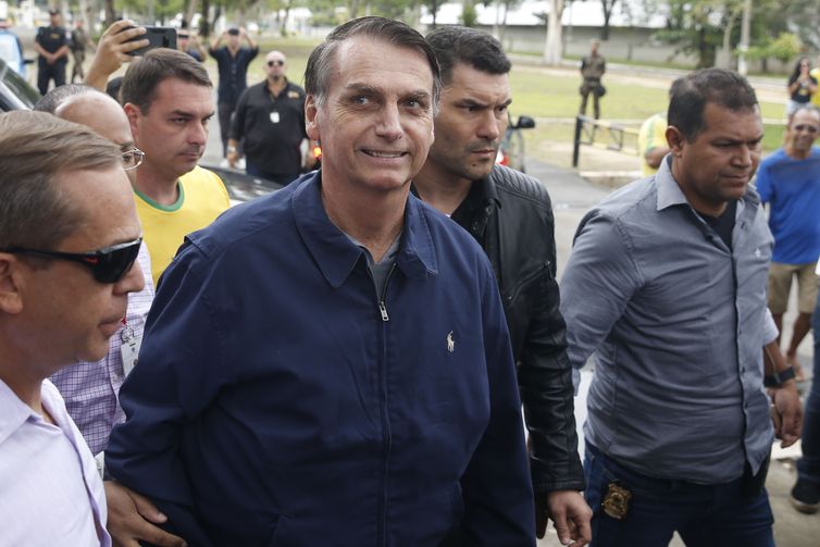 O candidato à Presidência Jair Bolsonaro (PSL) chega à seção eleitoral na Escola Municipal Rosa da Fonseca, na Vila Militar, acompanhado do filho Flávio Bolsonaro, que é candidato ao Senado. Agentes da Polícia Federal e militares do Exército