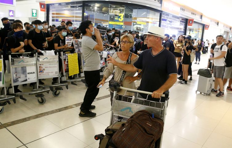 Passengers walk past anti-government protesters blocking the access to the departure gates, during a demonstration at Hong Kong International Airport, China August 13, 2019. REUTERS/Thomas Peter