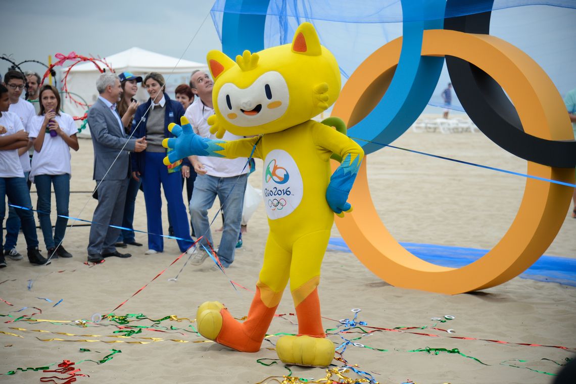 Tomaz Silva/Agência Brasil Mascote dos Jogos Rio 2016 posa diante da escultura dos aros olímpicos na Praia de Copacabana (Tomaz Silva/Agência Brasil)