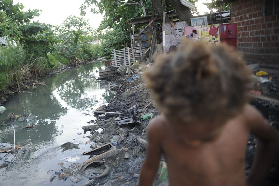 Imagem de riacho com falta de saneamento básico e uma criança passando em favela do Complexo da Maré