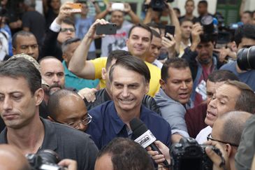 O candidato à Presidência Jair Bolsonaro (PSL) chega à seção eleitoral na Escola Municipal Rosa da Fonseca, na Vila Militar, acompanhado do filho Flávio Bolsonaro, que é candidato ao Senado. Agentes da Polícia Federal e militares do Exército