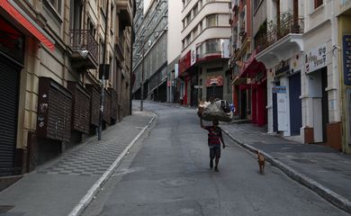 Um mendigo caminha com seu cachorro em uma rua vazia com lojas populares fechadas, no primeiro dia de um bloqueio imposto pelo governo do estado por causa do surto de doença por coronavírus (COVID-19)