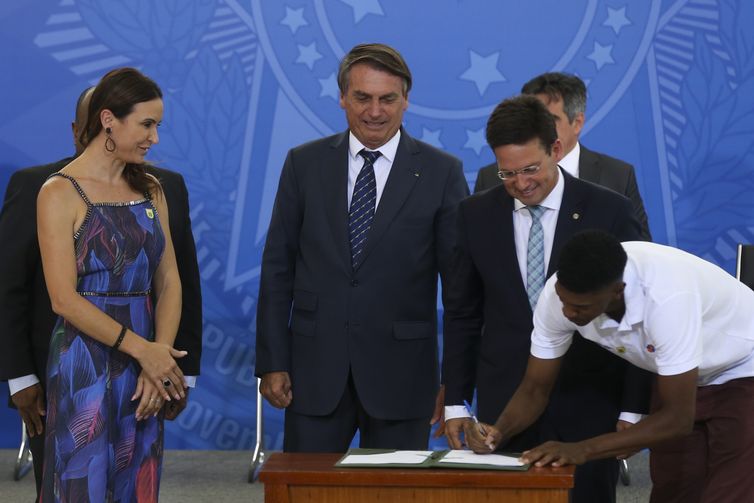 Antonio Cruz/Agência Brasil A atleta Maurren Maggi, o presidente da República, Jair Bolsonaro, o ministro da Cidadania, João Roma, e o atleta, André Domingos, participam da solenidade de assinatura do projeto de lei que institui o Plano Nacional do Desporto (PND), no