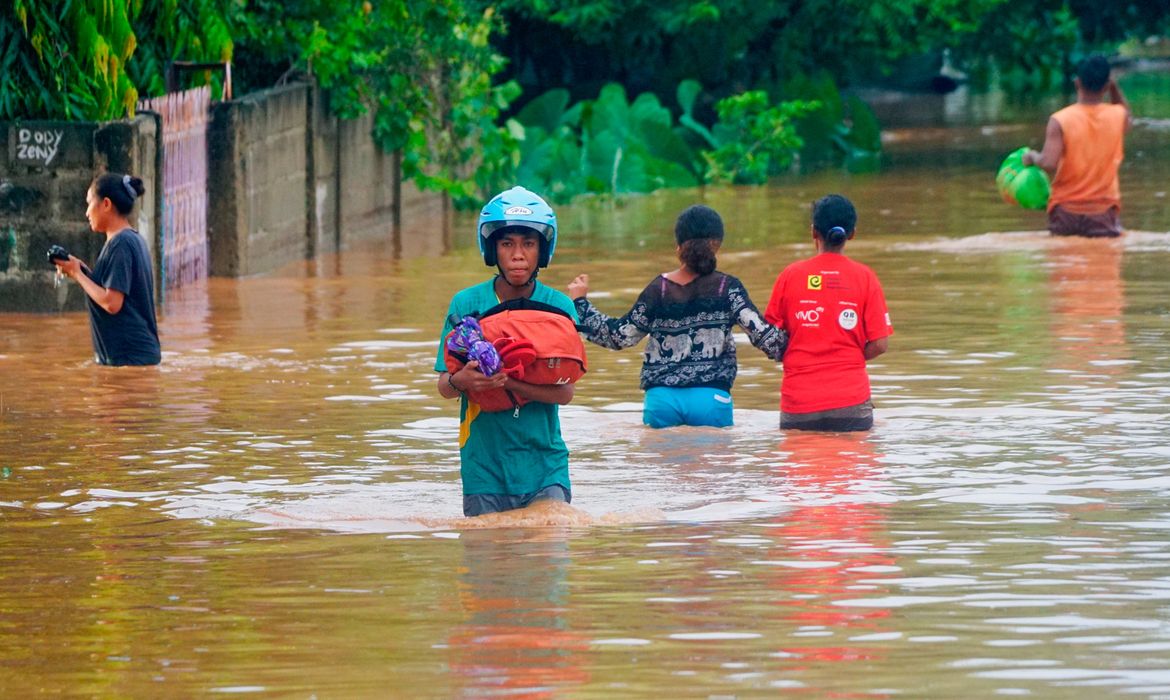 A man wearing a helmet carries his goods through the water in an area affected by floods after heavy rains in Dili