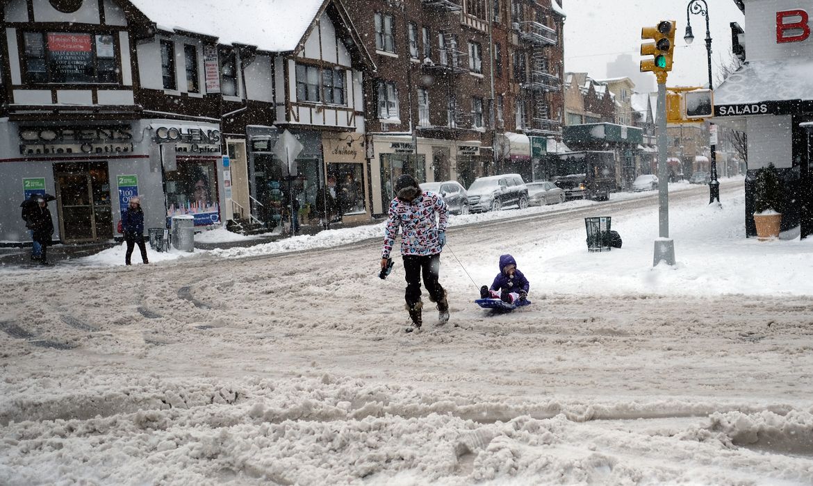 Mulher puxa trenó de criança aproveitando a neve acumulada nas ruas de Nova York