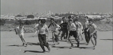 Crianças jogam futebol próximo a uma fábrica