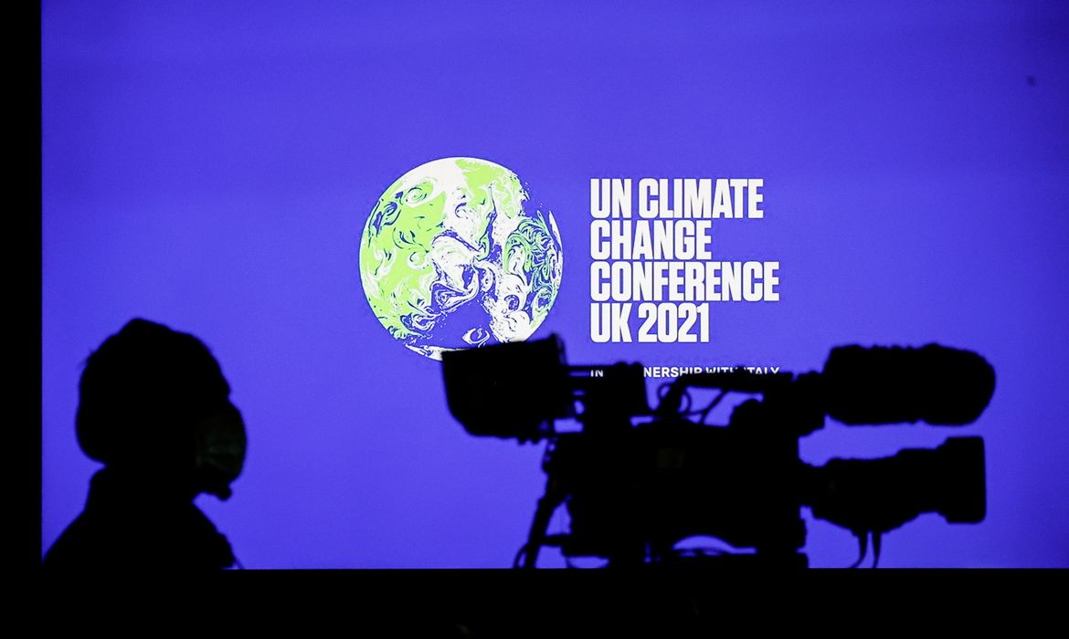 Cinegrafista em frente ao logo da COP26 durante entrevista coletiva em Glasgow