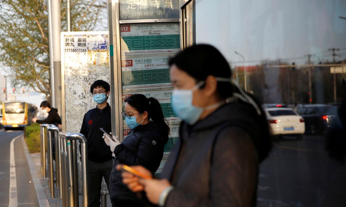 People wearing face masks wait for buses at a bus stop, as the country is hit by an outbreak of the novel coronavirus disease (COVID-19), in Beijing