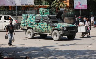 SENSITIVE MATERIAL. THIS IMAGE MAY OFFEND OR DISTURB  A man walks near a body while a military vehicle patrols after the government declared a state of emergency amid violence, in Port-au-Prince, Haiti, March 4, 2024. REUTERS/Ralph Tedy Erol