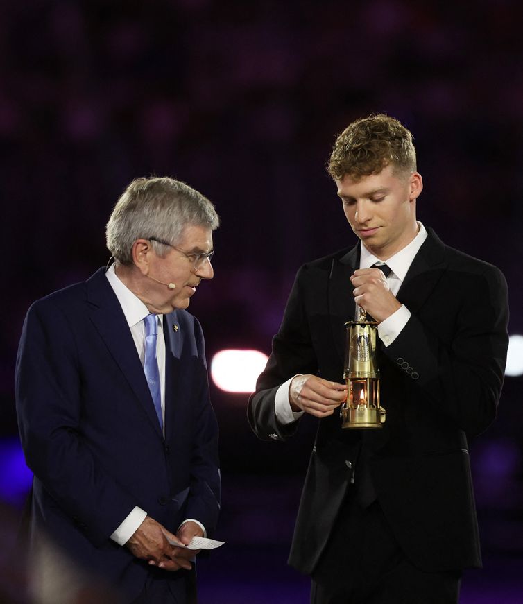 Paris 2024 Olympics - Ceremonies - Paris 2024 Closing Ceremony - Stade de France, Saint-Denis, France - August 11, 2024. Leon Marchand of France holds the Olympic flame as International Olympic Committee (IOC) President Thomas Bach looks on. REUTERS/Phil Noble