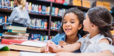 Duas crianças estudam em uma biblioteca