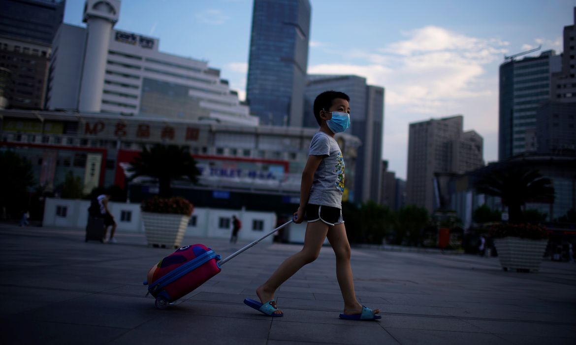 Menino de máscara protetora caminha perto da Estação Ferroviária de Xangai