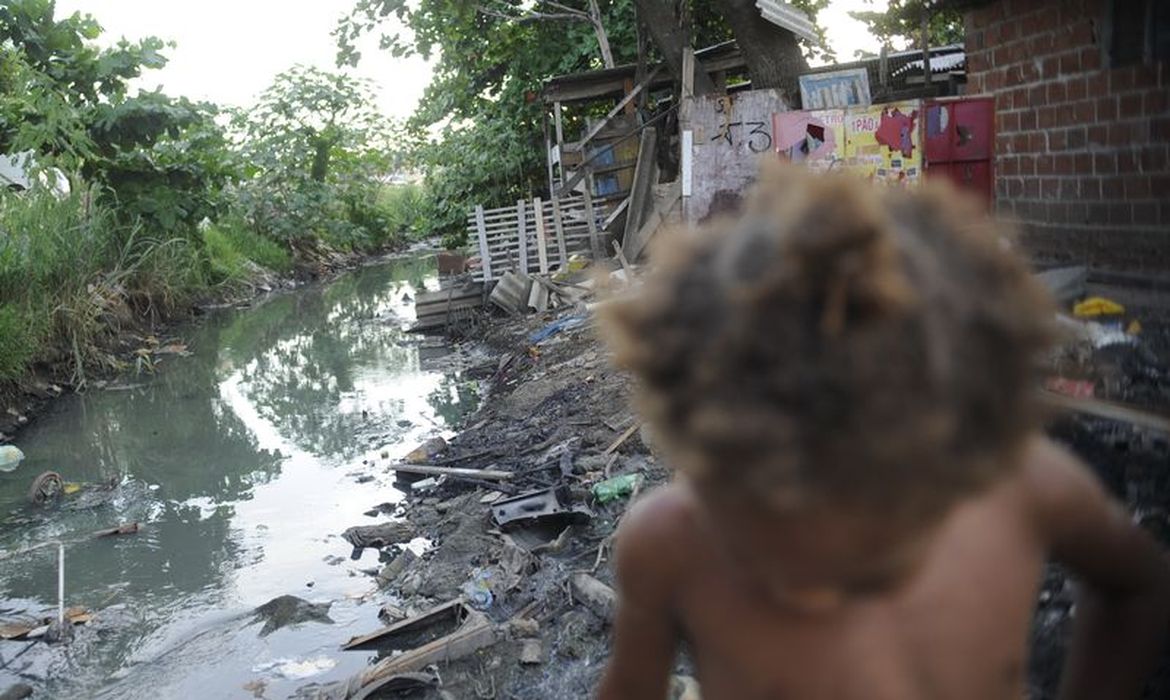Imagem de riacho com falta de saneamento básico e uma criança passando em favela do Complexo da Maré