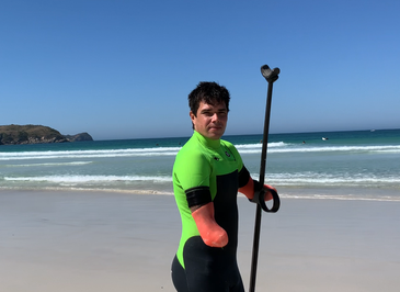 Praia. Na areia, Jonas com o coto esquerdo encaixado em uma das argolas de um remo.