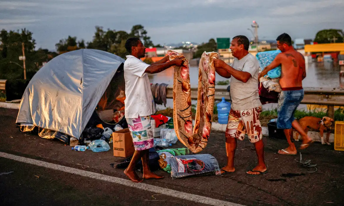 Men fold a blanket as they camp on the road near a flooded street in Eldorado do Sul, in Rio Grande do Sul, Brazil, May 6, 2024. REUTERS/Amanda Perobelli