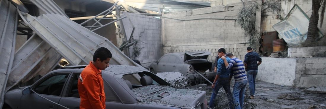 Cidadãos palestinos observam um carro perto da agência do Banco Nacional Islâmico, após um ataque aéreo de Israel