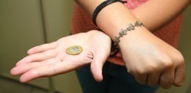 Pessoa mostra moeda em mão aberta cruzada com a outra, que está fechada