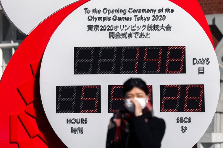 A woman wearing a protective face mask, following an outbreak of the coronavirus, stands in front of the big Omega One-Year Countdown clock for the opening ceremony of the Tokyo 2020 Olympic outside of Tokyo Station in Tokyo