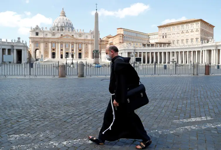 REUTERS / Guglielmo Mangiapane/Direitos Reservados Frei usa máscara de proteção ao passar por Praça de São Pedro deserta no Vaticano