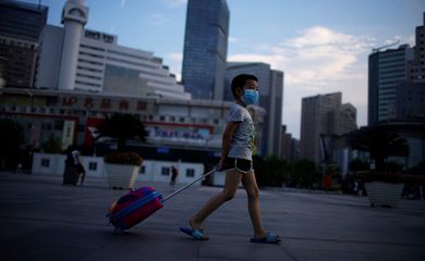 Menino de máscara protetora caminha perto da Estação Ferroviária de Xangai