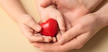 Mãos de adulto envolvem mãos de criança que segura um coração
