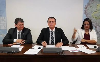 O presidente Jair Bolsonaro faz transmissão ao vivo ao lado do ministro da Infraestrutura, Tarcísio Gomes de Freitas, e da intérprete de libras, Elizângela Castelo Branco.