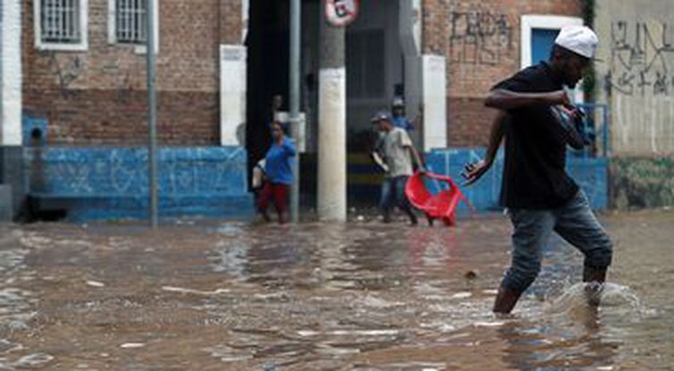 Pessoas caminham por uma rua inundada após fortes chuvas no bairro de Vila Prudente, em São Paulo.