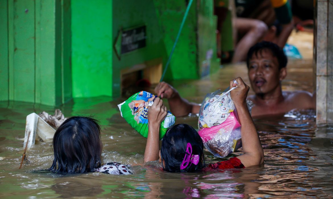 Mulheres atravessam uma área inundada após fortes chuvas em Jacarta, na Indonésia.