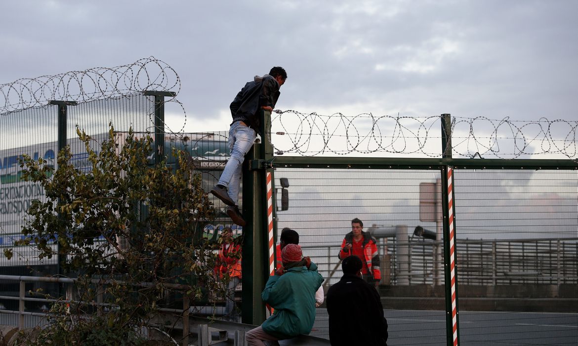 Imigrantes em Calais, na França, escalam uma cerca na tentativa de embarcar em um trem para a Inglaterra