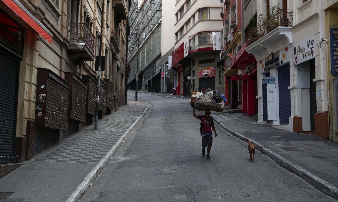 Um mendigo caminha com seu cachorro em uma rua vazia com lojas populares fechadas, no primeiro dia de um bloqueio imposto pelo governo do estado por causa do surto de doença por coronavírus (COVID-19)