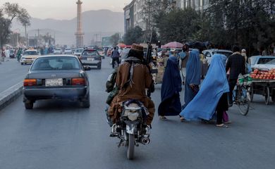 FILE PHOTO: A group of women wearing burqas crosses the street as members of the Taliban drive past