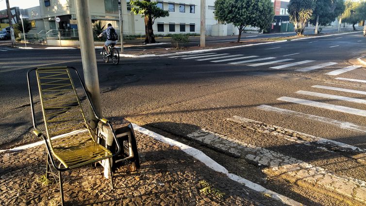 Rua remota durante a pandemia. 
No primeiro plano da foto, cadeira de balanço e faixas de pedestre. Ao fundo, ciclista solitário em uma rua vazia.