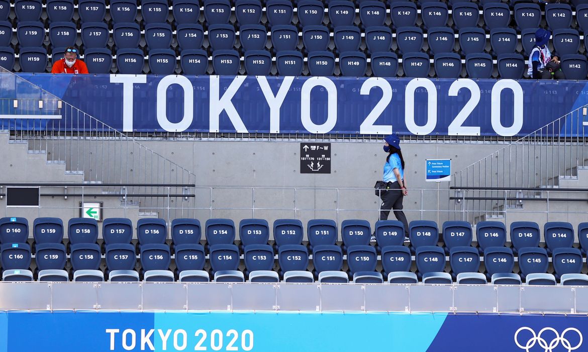 Espectadora caminha embaixo de placa da Tóquio 2020 no estádio onde é disputado o torneio olímpico do hóquei - arquibancada vazia - Tóquio 2020 