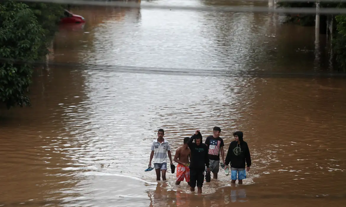 Pessoas caminham por uma rua inundada após fortes chuvas no bairro de Vila Prudente, em São Paulo. 