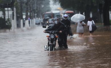 Um homem empurra uma motocicleta por uma rua inundada após fortes chuvas no bairro Butanta, em São Paulo

