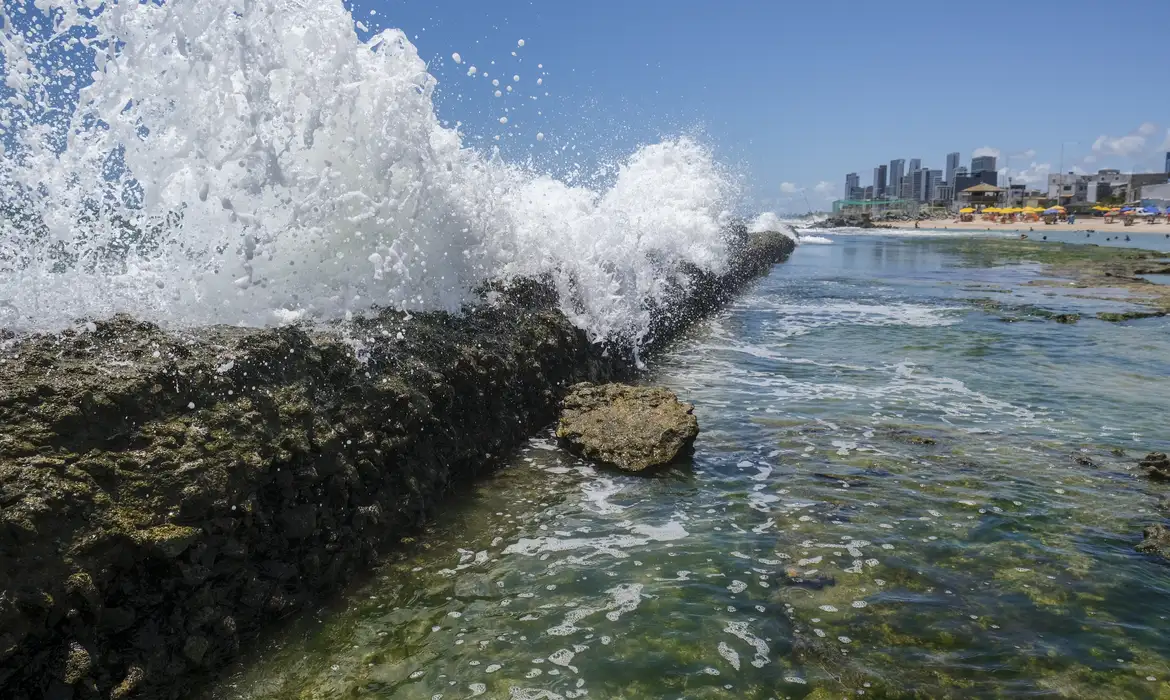 Recife(PE), 24/10/2023 - Explosão de ondas nos recifes costeiros na praia do Buraco da Véia, com a orla de Boa Viagem ao fundo, funcionando como barreira natural. As formações rochosas absorvem até 96% do impacto das ondas.  Foto: Fernando Frazão/Agência Brasil