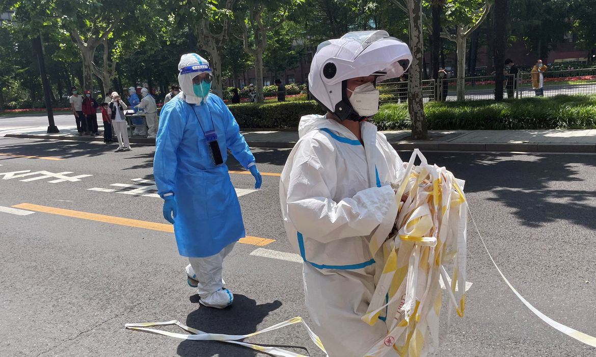 Funcionário em trajes de proteção remove cordão de isolamento de área residencial em Xangai, na China