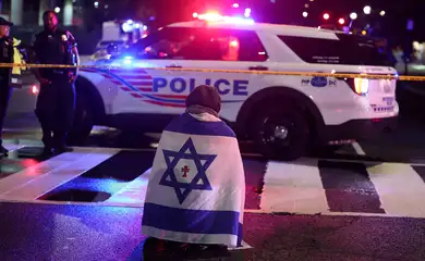 A man, with an Israeli flag with a cross in the center, kneels next to emergency personnel working at the site where, according to the U.S. Homeland Security Secretary, two Israeli embassy staff were shot dead near the Capital Jewish Museum in Washington, D.C., U.S. May 21, 2025.  REUTERS/Jonathan Ernst    TPX IMAGES OF THE DAY
