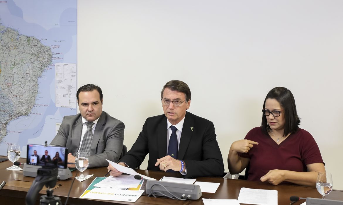 O presidente Jair Bolsonaro faz transmissão ao vivo ao lado do ministro da Secretaria-Geral da Presidência, Jorge Francisco, e da intérprete de libras, Elizângela Castelo Branco.