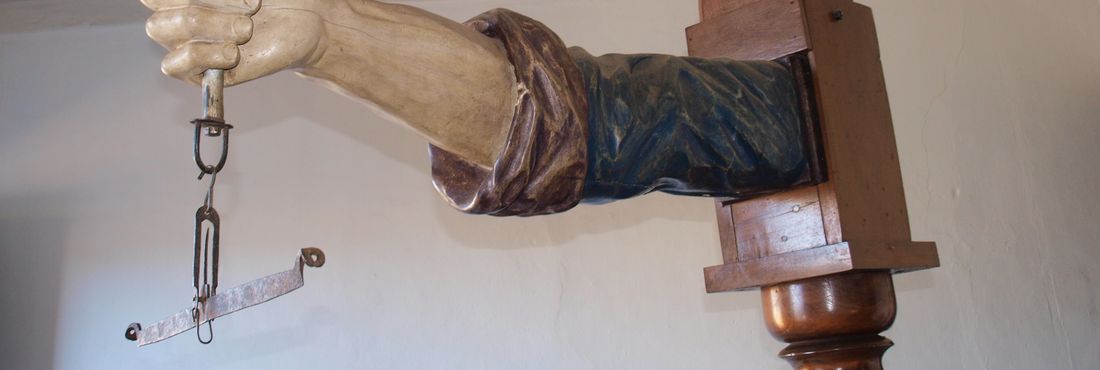 "Braço de justiça", peça do Museu Tomé Portes Del-Rei. O braço esculpido em madeira integrava a balança de arrecadação do quinto do ouro. Vinda de Portugal, a peça era usada na Casa de Fundição de São João del-Rei, no século XVIII.