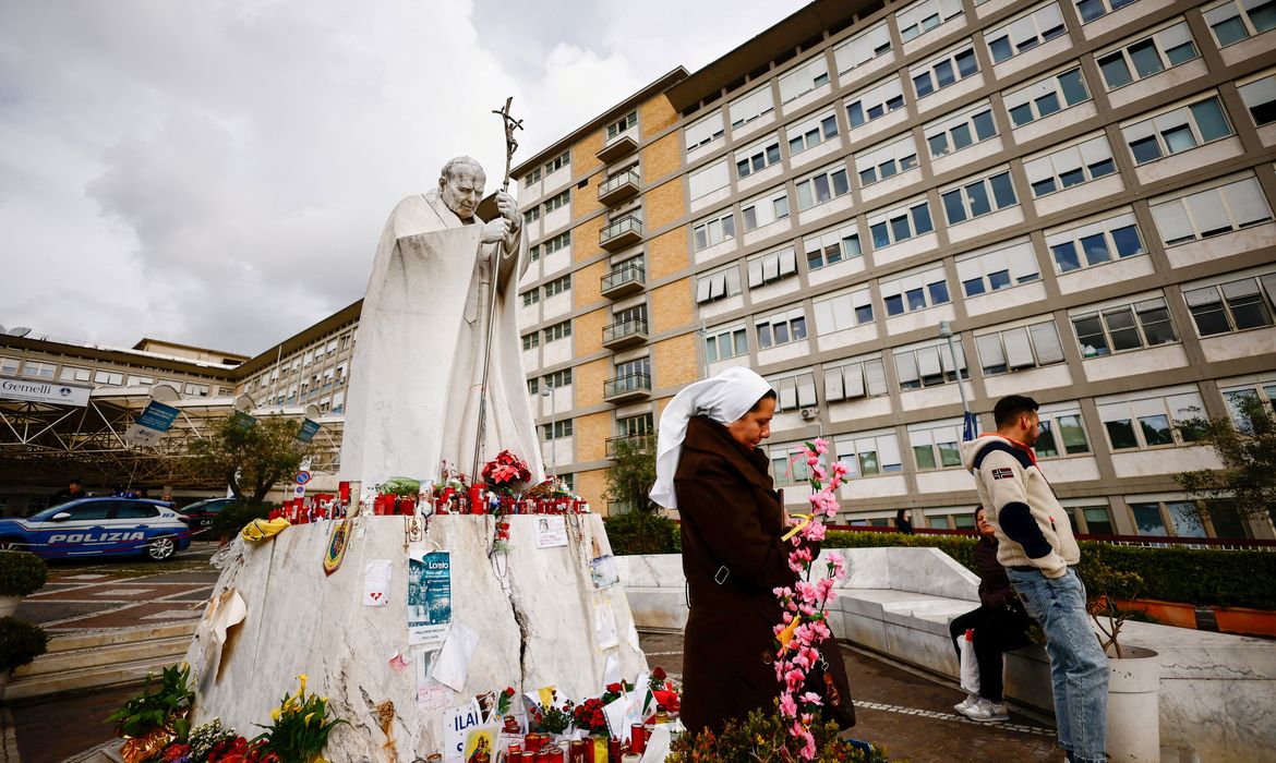 People stand near the statue of late Pope John Paul II outside Gemelli Hospital, where Pope Francis is admitted for ongoing pneumonia treatment, in Rome, Italy, March 13, 2025. REUTERS/Yara Nardi