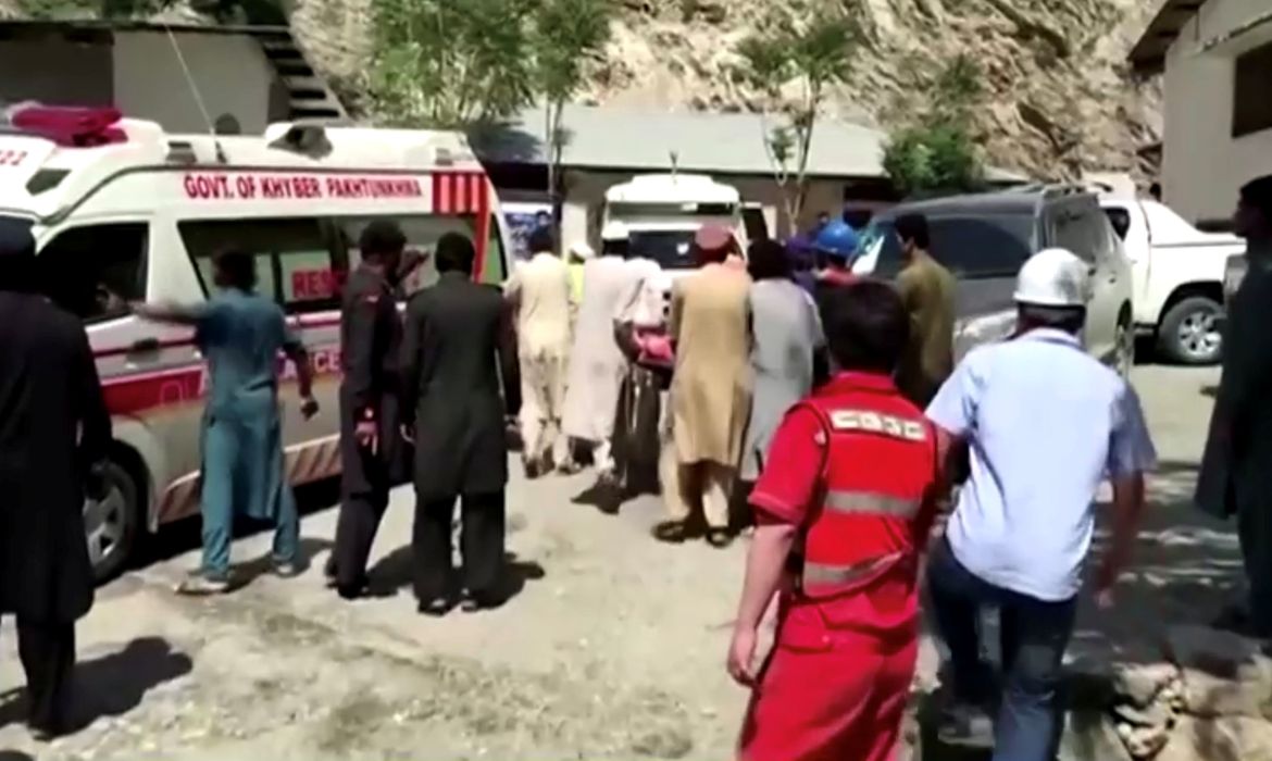 Pessoas colocam maca em ambulância do lado de fora de hospital em Dasu, no Paquistão, após explosão de ônibus