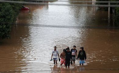 Pessoas caminham por uma rua inundada após fortes chuvas no bairro de Vila Prudente, em São Paulo. 