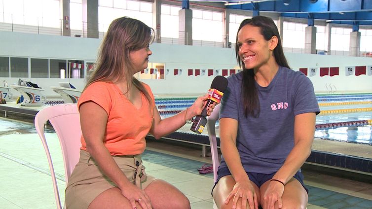 Sentadas lado a lado, Fernanda Honorato com o microfone do Programa Especial, na mão esquerda, direcionado para Maria Carolina