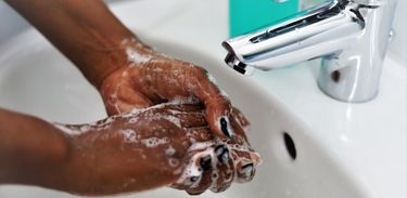 Mulher lava as mãos com sabonete; close nas mãos